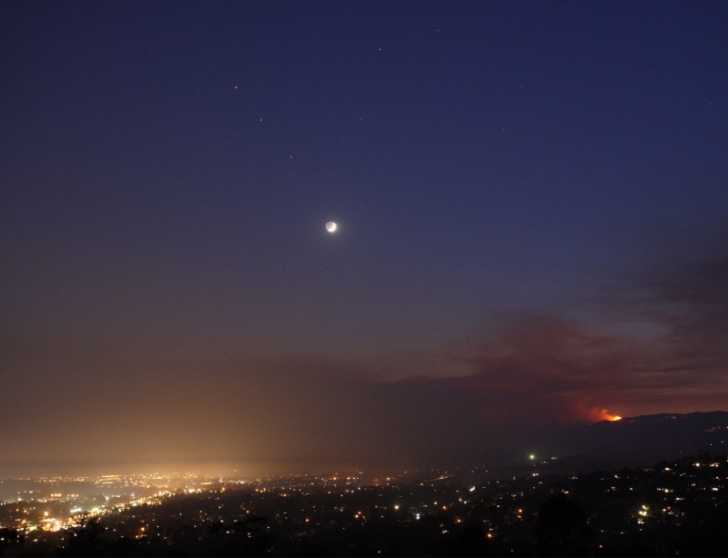 Über Santa Barbara in Kalifornien leuchtet der junge Sichelmond am Himmel, den das Altlicht zu einer vollständigen Kugel macht. Hinter dem Horizont brennt Feuer.