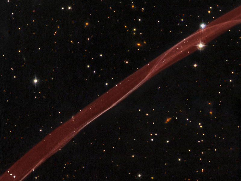 Ein rötliches Band verläuft diagonal von links unten nach rechts oben durch ein Sichtfeld mit einigen verstreuten Sternen.
