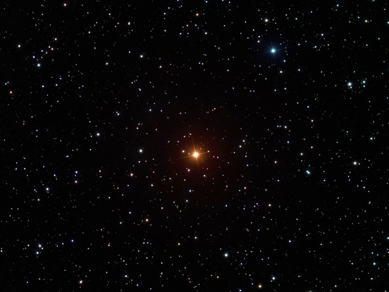 In der Mitte eines Sternfeldes leuchtet ein orangefarbener Stern.