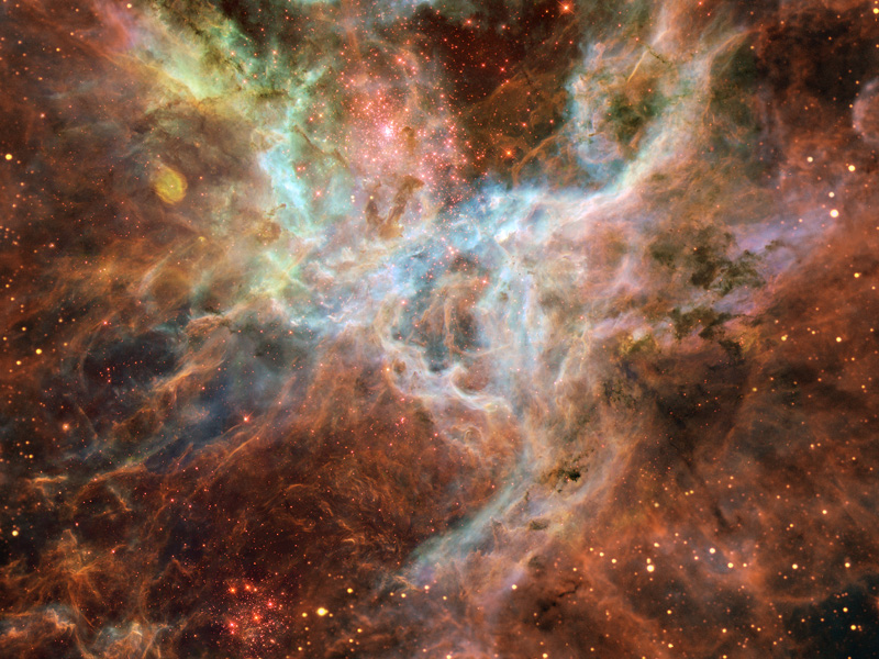 Das Bild zeigt einen stark strukturierten, fasrigen Nebel mit wenigen Sternen, in rötlichen und grün-weißlichen Farben.
