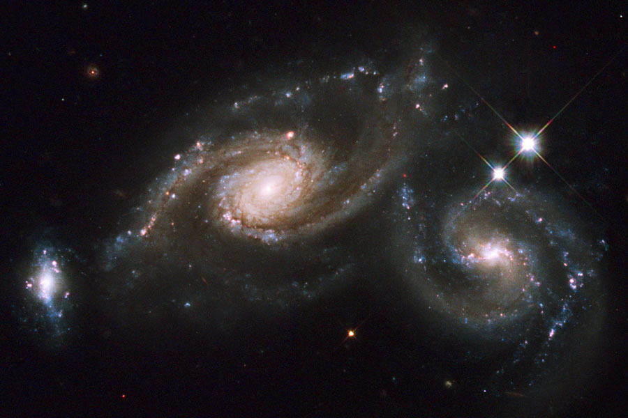 Zwei Galaxien kollidieren, sie haben sehr lose, verzerrte Spiralarme. Links unten ist eine dritte, kleinere Galaxie.