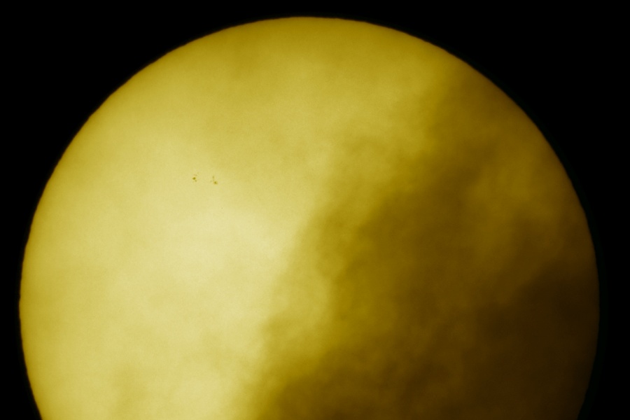 Die unten angeschnittene, gelbe Sonne ist rechts von Wolken bedeckt, auf der Oberfläche sind wenige sehr kleine Flecken zu sehen.