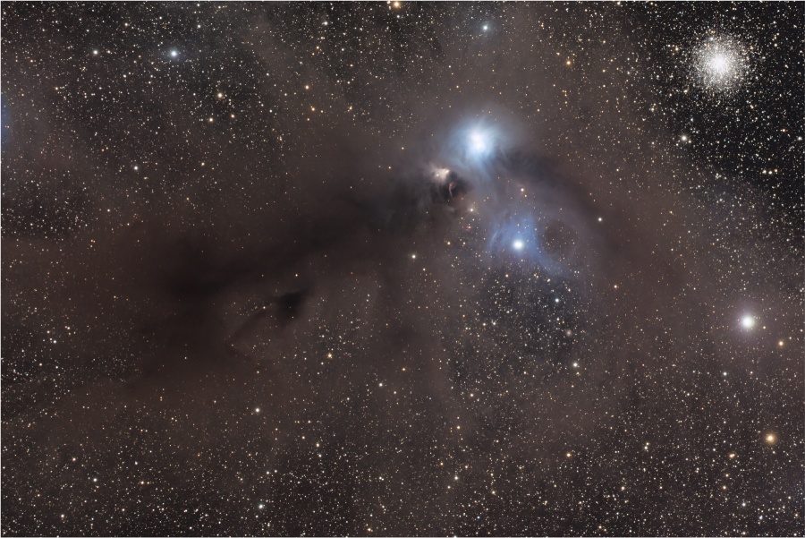 Links unten ist ein Dunkelnebel, in der Mitte leuchten zwei Sterne, die von blauen Nebeln umgeben sind, und rechts oben ist ein Kugelsternhaufen.