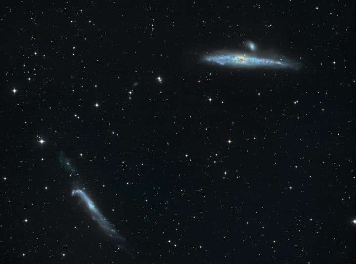 Links unten und rechts oben leuchten zwei bläuliche Galaxien im Bild, umgeben von Sternen.