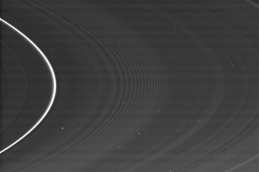 Das BIld zeigt die rillenförmigen Saturnringe in hoher Auflösung. Links ist ein sehr heller einzelner Ringbogen, die restlichen Ringe sind sehr blass. Dazwischen sind einige kleine helle Punkte verteilt.