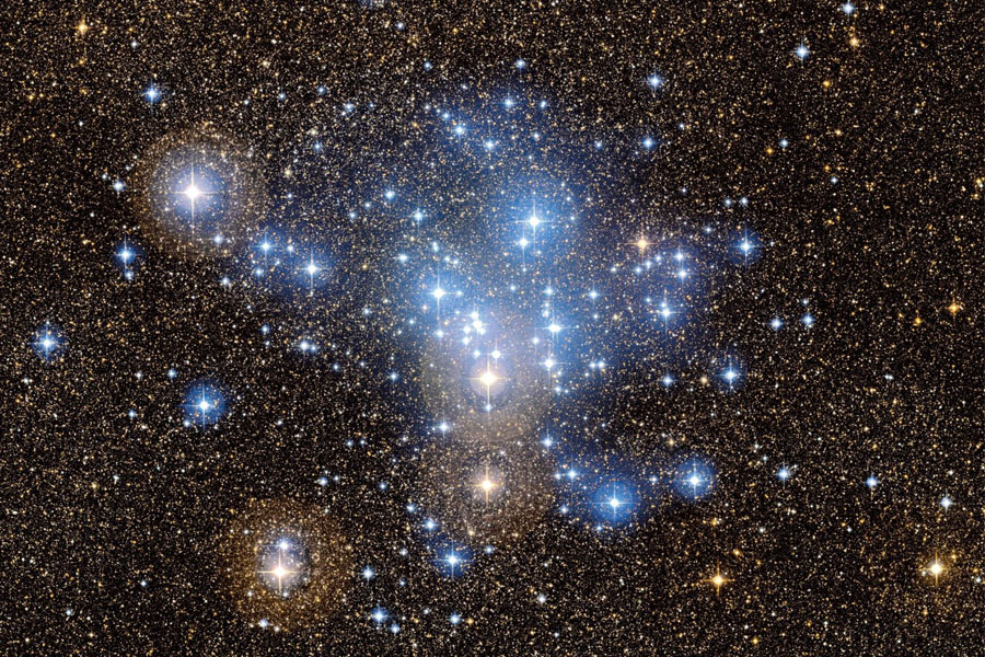 Das Bild zeigt einen offenen Haufen aus Sternen, die von einem blauen Schimmer umgeben sind.