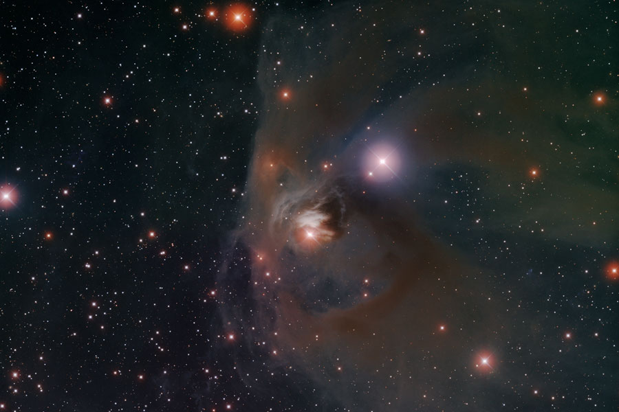 In der Bildmitte leuchtet ein orangefarbener, von Nebeln umgebener Stern, es ist T Tauri im Sternbild Stier.