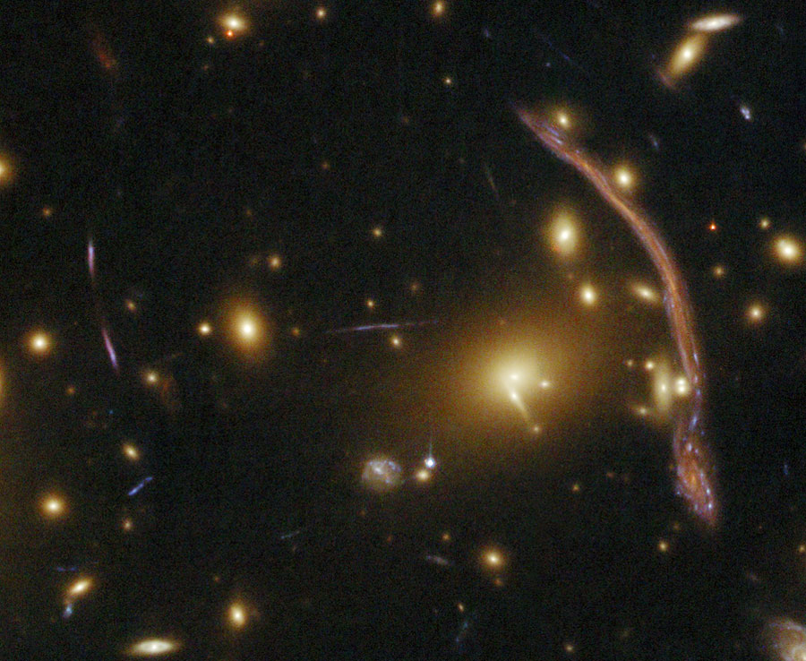 Im Bild sind viele Galaxien lose verteilt, auf der rechten Seite ist ein senkrechter Bogen, eine verzerrte Galaxie.