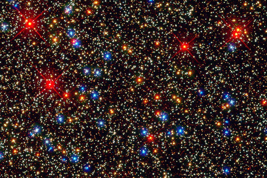 In einem dicht gedrängten Sternenfeld stechen rot umrandete und blau leuchtende Sterne heraus.