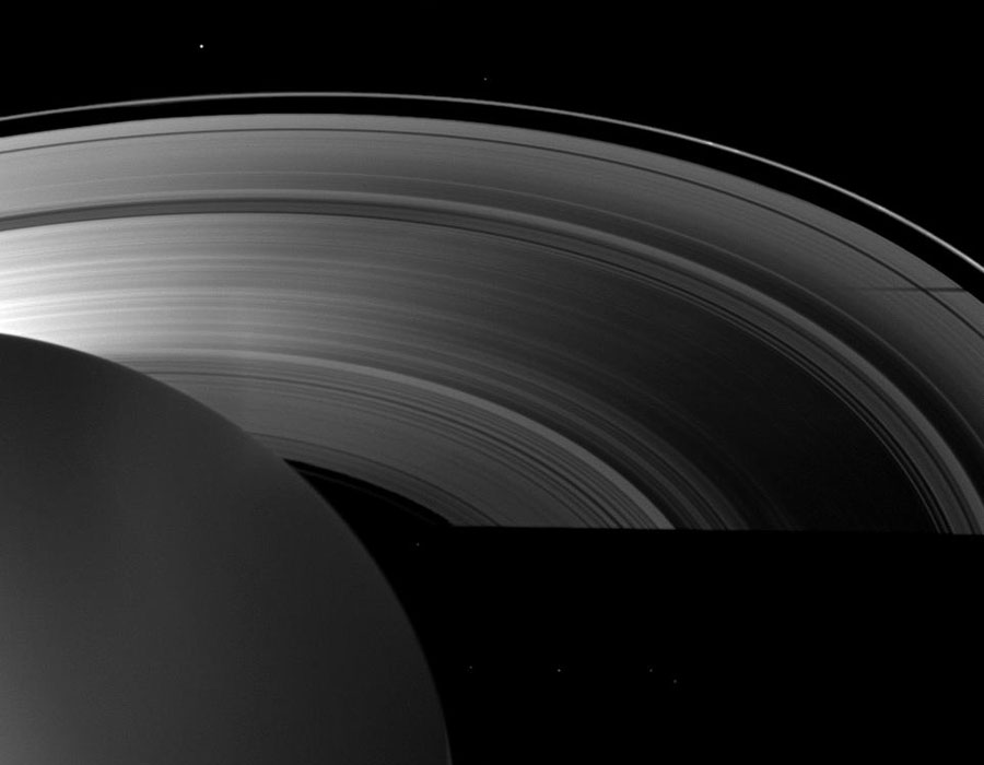 Links unten zeichnet sich der dunkle Körper des Planeten Saturn ab, darum biegen sich die Ringe, die von links beleuchtet sind. Der Planeten wirft rechts seinen Schatten auf die Ringe. Die Teilungen und Strukturen sind gut erkennbar.