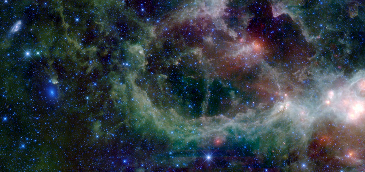 Der Herznebel bildet eine ausladende grünliche Staubranke mitten im Bild, rechts leuchten einige helle Flecke, links sind zwei Galaxien erkennbar.