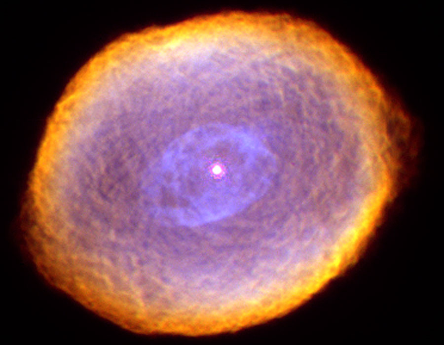 Der bildfüllende, leicht ovale Nebel hat eine Struktur ähnlich wie ein Häkeldeckchen.Er ist innen mattviolett und geht am äußeren Rand in Gelb, Orange und Rot über.