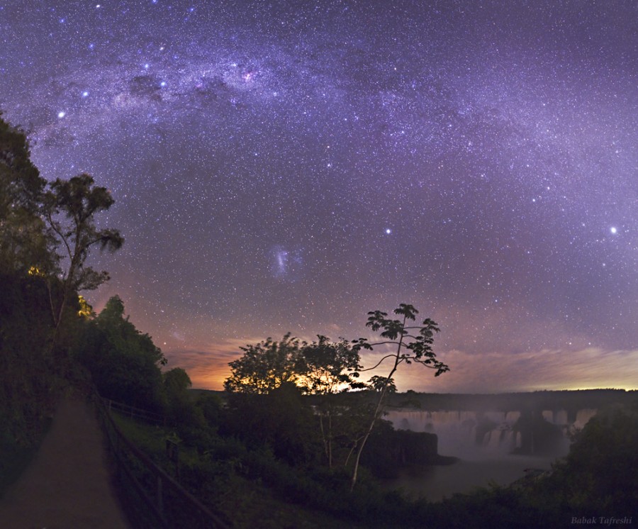 Über einer Nachtlandschaft wölbt sich die Milchstraße am sternklaren Himmel, darunter die Magellanschen Wolken.
