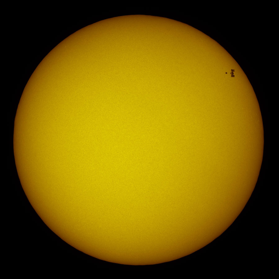 Die abgebildete Sonne ist sehr gleichmäßig und hat einen abgedunkelten Rand. Rechts oben ist ein dunkler Fleck, es sind die Internationale Raumstation und die Raumfähre Atlantis.