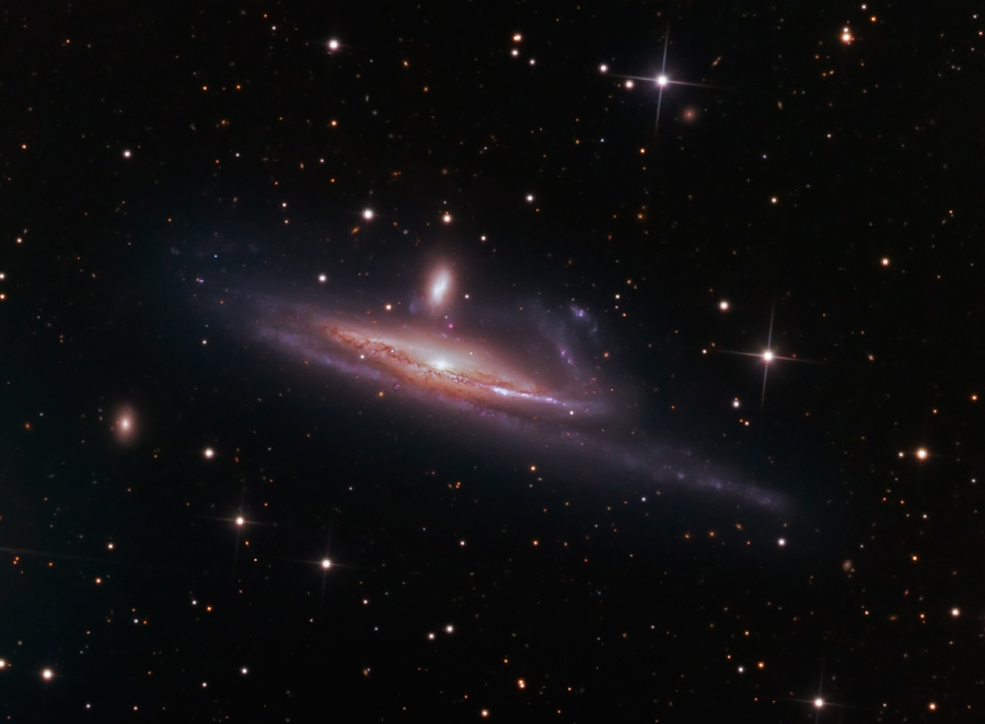 Mitten im Bild schwebt eine schräg von der Seite sichtbare Spiralgalaxie, darüber ist eine kleinere Galaxie. Rundum sind wenige Sterne verteilt.