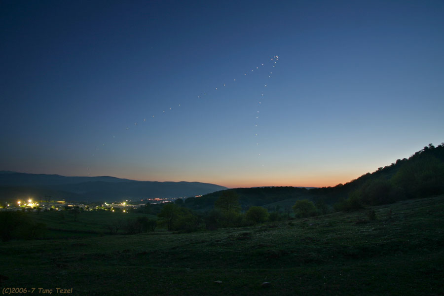 Am kristallklaren Himmel nach Sonnenuntergang leuchtet die Venus. Im Vordergrund ist die Silhouette einer Landschaft, links sind die Lichter einer Siedlung zu sehen.