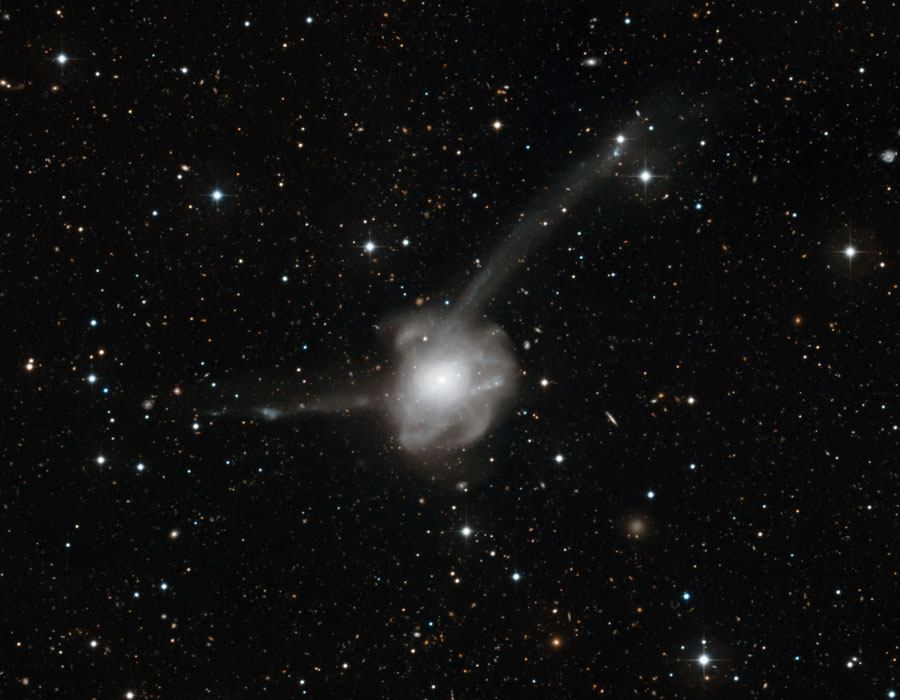 Mitten im Bild, in dem Sterne gleichmäpig verteilt sind, leuchtet ein weißes Knäul von dem nach links und rechts oben Sternströme auslaufen.