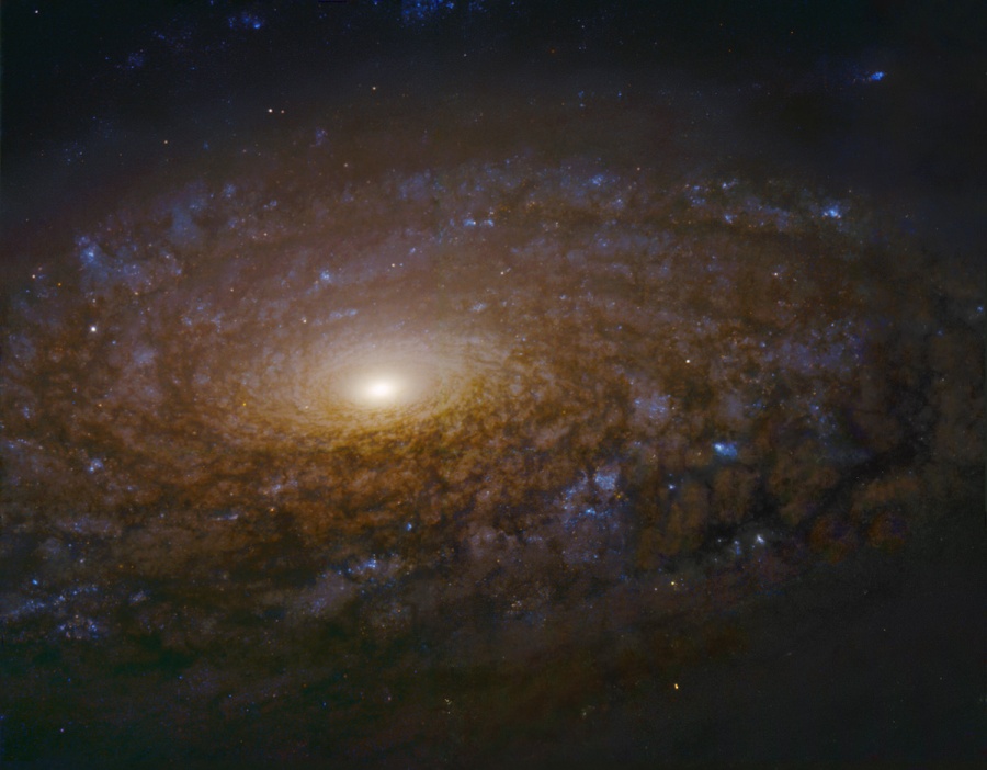 Vor uns breitet sich ein dunkler Wirbel einer Spiralgalaxie aus, der zu einem helle Zentrum in der Bildmitte führt.