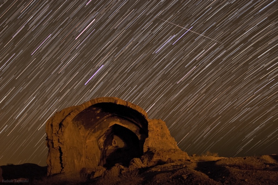 Hinter einer alten Zisterne der historischen Stadt Qumis ziehen Sterne ihre Strichspuren, oben blitzt ein Meteor durchs Bild.