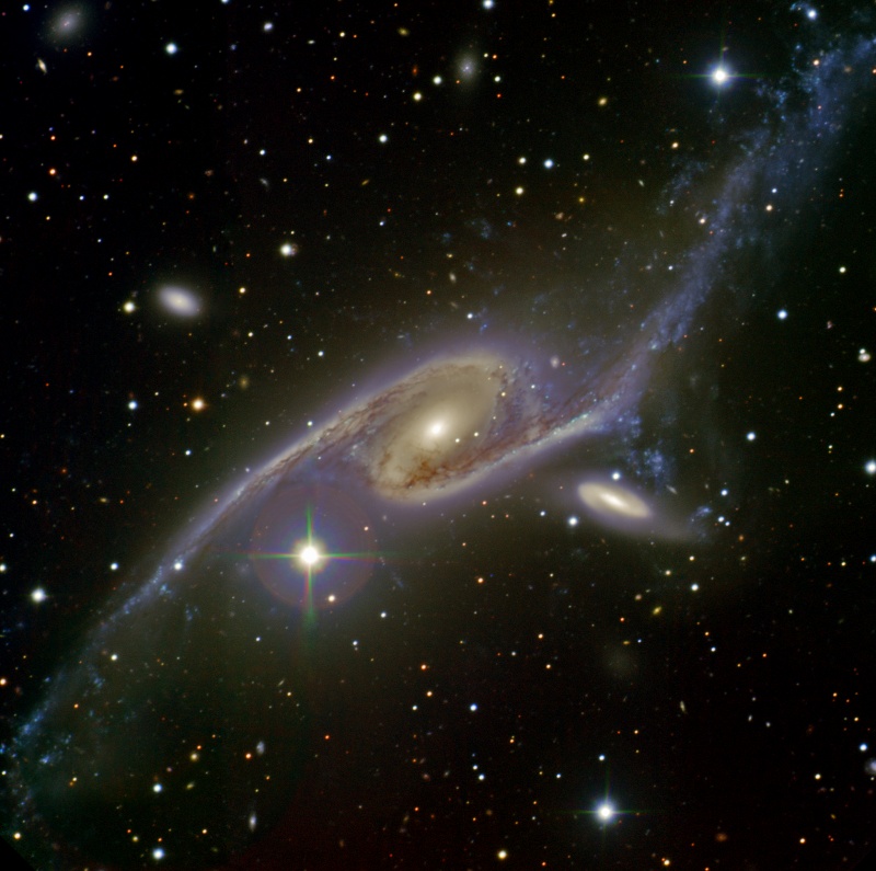Die größere Galaxie im Bild ist stark in die Länge gezogen, nach links unten und rechts oben verlaufen lange Spiralarme. Rechts hinter der Galaxie schwebt eine kleinere Spiralgalaxie.
