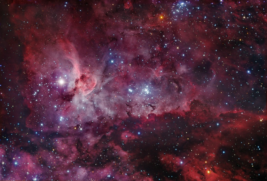 Der rot leuchtende Carinanebel ist stark strukturiert, davor sind Sterne unterschiedlich dicht verteilt.
