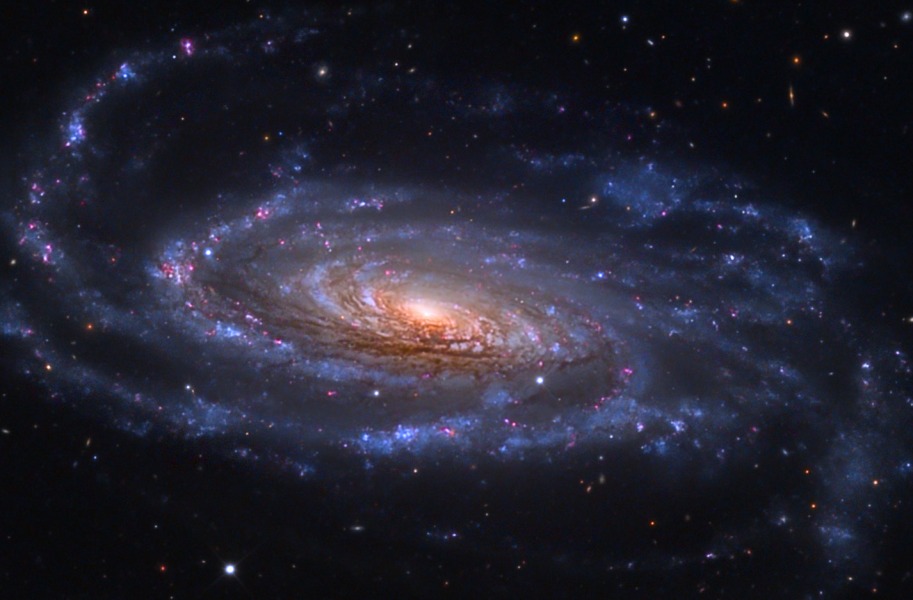 Eine lose gewundene Spiralgalaxie mit vielen rosaroten Sternbildungsregionen und blauen Sternhaufen ist schräg von oben zu sehen. Ihre Schwibe macht einen leicht verkrümmten Eindruck.
