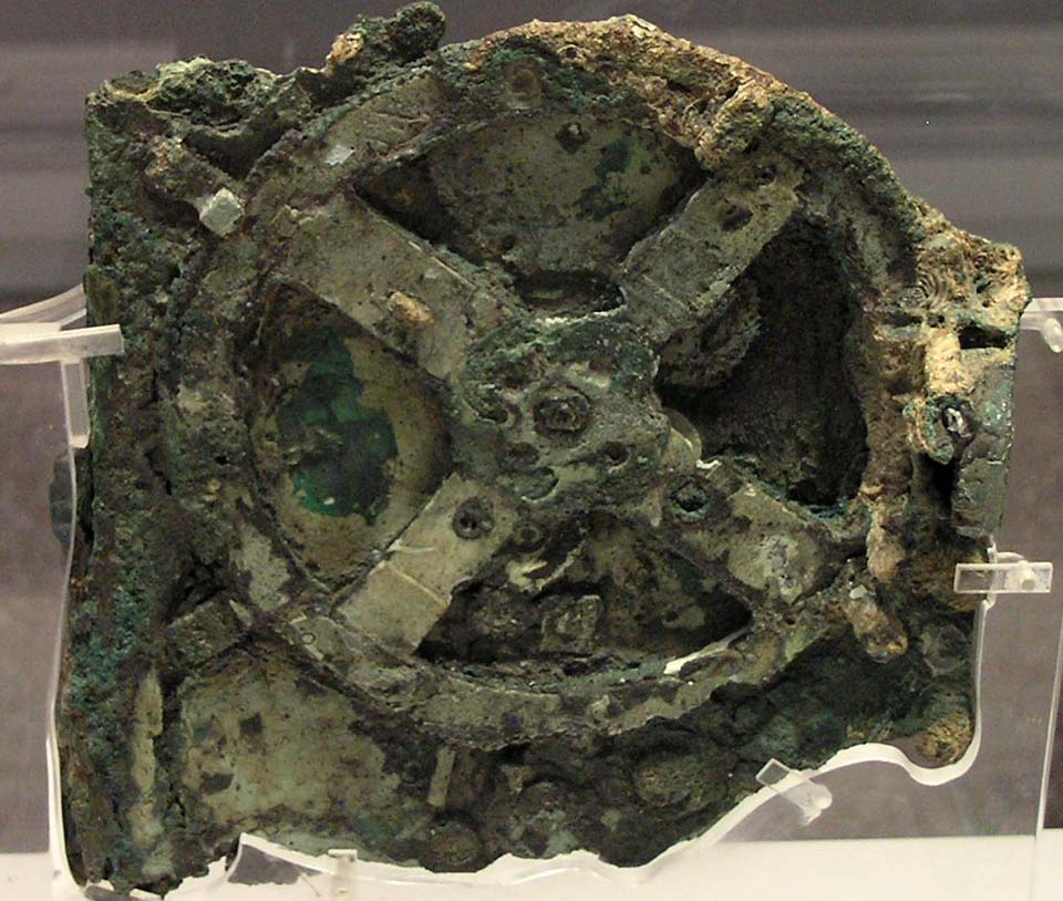 Das Bild zeigt ein stark korrodiertes Rad mit vier Achsen, das Fragment hat einen grünlichen Farbton.