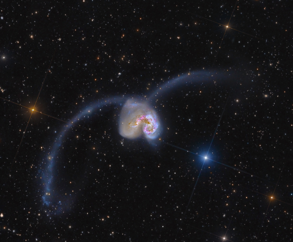 In der Mitte sind zwei Galaxien eng beisammen, nach links und rechts sind zwei Schweife aus Sternen in Bögen hinausgeschleudert.