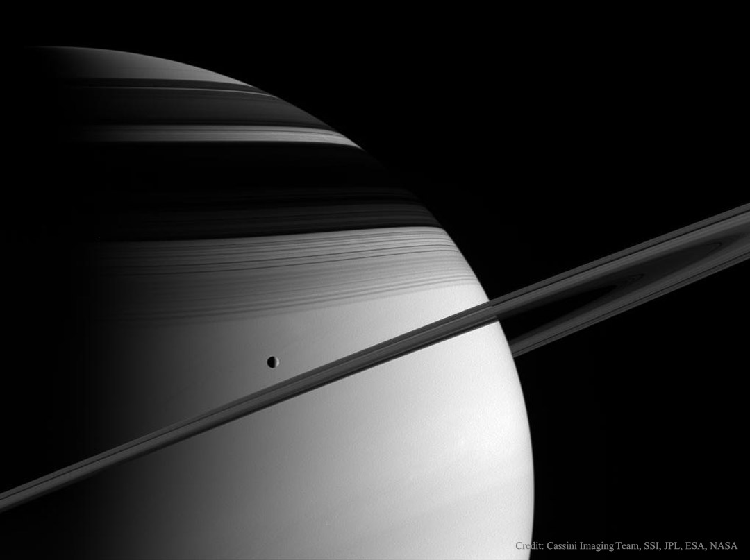 Die Raumsonde Cassini zeigt den Mond Tethys vor dem Gasriesen Saturn mit Ringen und Schatten.