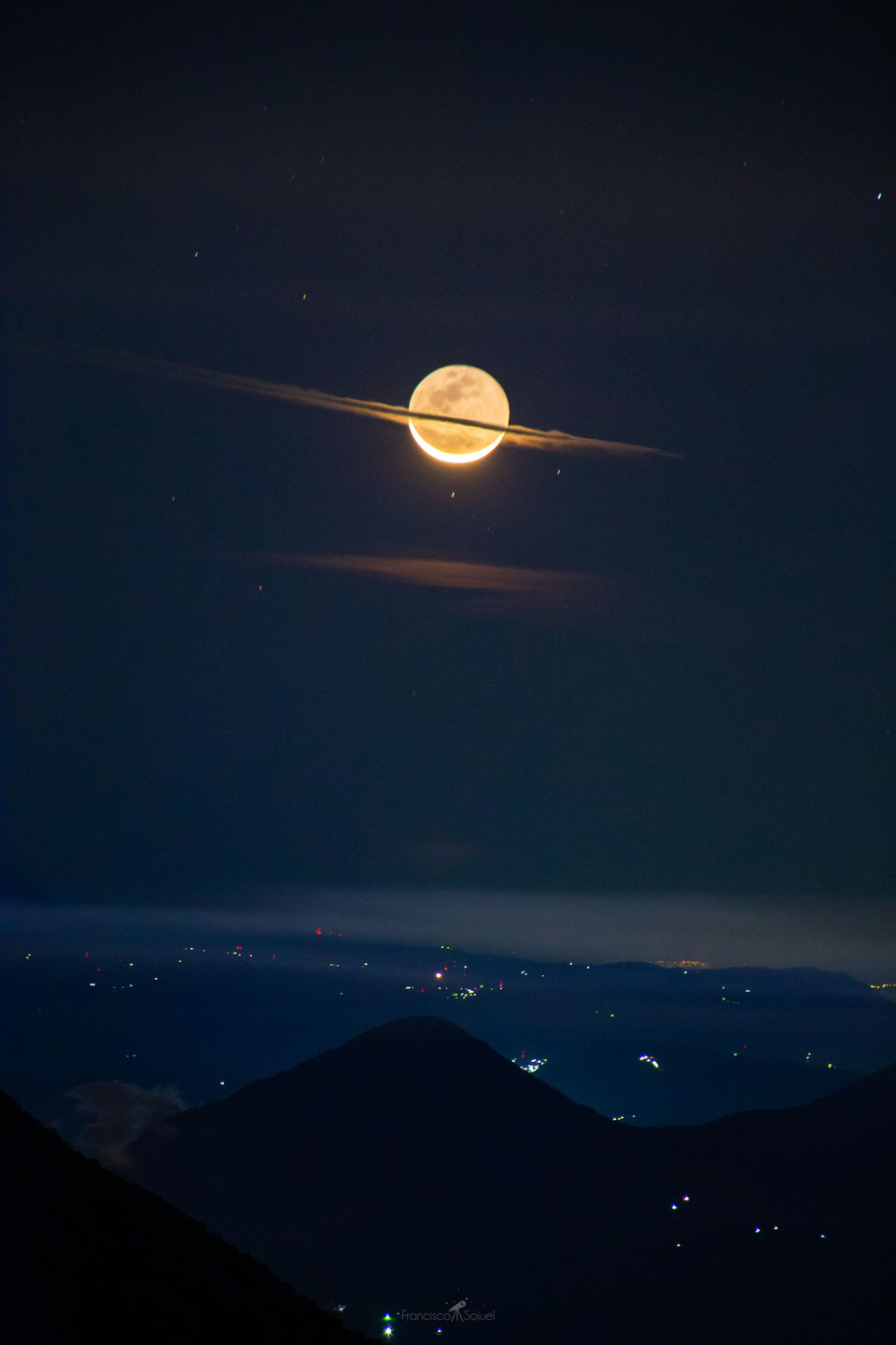 Das Bild zeigt den Mond am Nachthimmel der Erde hinter einem Wolkenstreifen, sodass er aussieht wie ein riesiger Saturn.