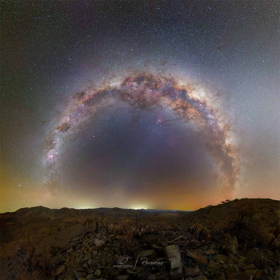 Das Bild zeigt einen Ring aus Sternen, dieser ist eine Projektion des Zentralbands unserer Milchstraße. Im Vordergrund sind Felsen und Kakteen aus der Hochwüste in Chile zu sehen.