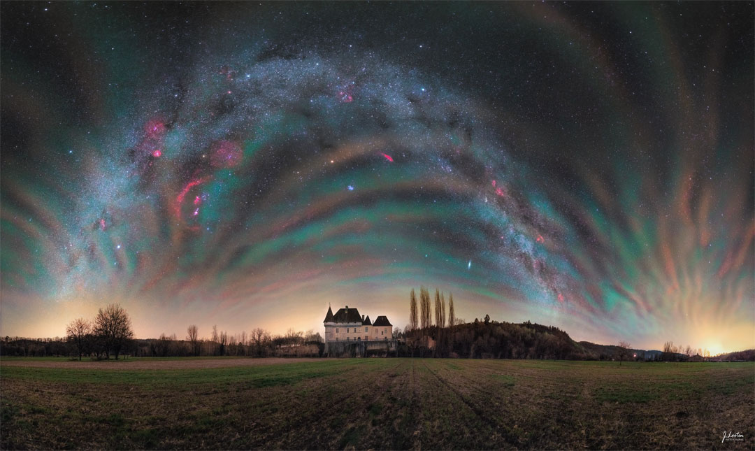 Das Bild zeigt den farbenprächtigen Himmel mit Nachthimmellicht über einem Schloss in Frankreich. Im Hintergrund sind Objekte zu erkennen sind Objekte wie der Orionnebel, Sirius, Mars und ein und das gewölbte Band unserer Milchstraße.