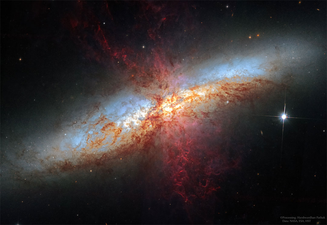 Die Galaxie im Bild ist sehr unregelmäßig, sie verläuft diagonal durchs Bild, ist von der Seite zu sehen und im Vordergrund ist ein rot gefleckter Nebel.