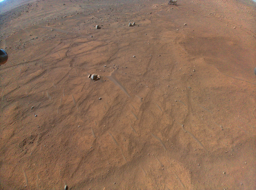 Der Marshelikopter Ingenuity zeigt seine Aussicht 5 Meter über dem Marsboden. Oben hinten ist der untere Teil des Marsrovers Perseverance zu sehen.