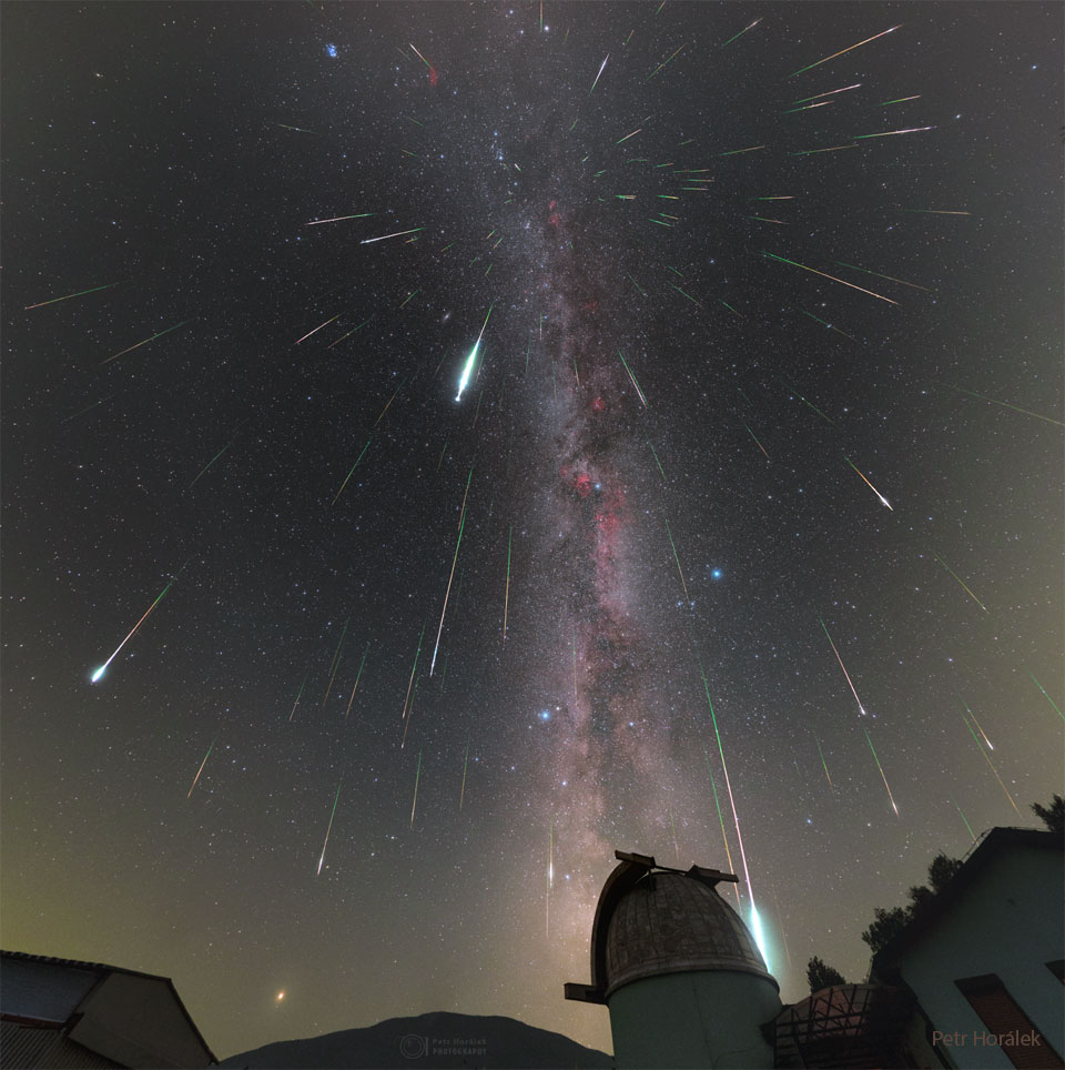 Hinter der Silhouette einer Sternwartekuppel zischen Meteore über den dunklen Nachthimmel. Im Hintergrund ist die Milchstraße zu sehen.