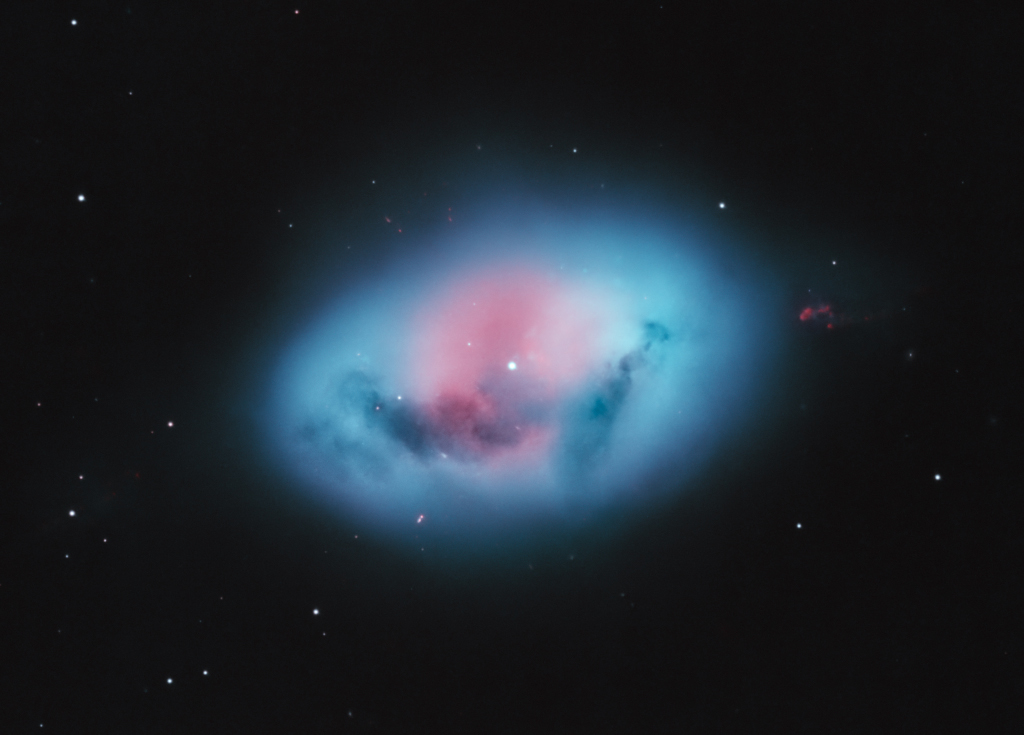 In der Mitte des Bildes liegt ein blauer eiförmiger Nebel, leicht verschwommen, um den hellen Stern in der Mitte leuchtet er rötlich.