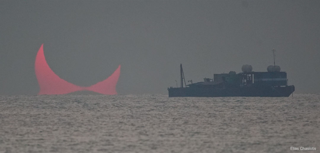 Am Horizont eines Meeres ist rechts ein Schiff zu sehen, links geht eine sichelförmige, matte rote Sonne auf, die stark verzerrt ist.