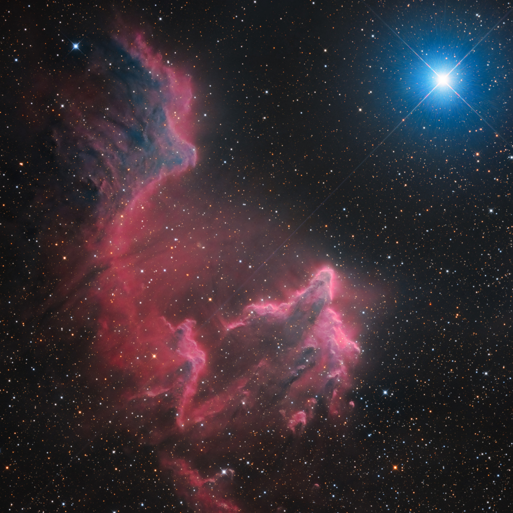 Rechts oben leuchtet ein blauer Stern mit Zacken, von links oben breitet sich nach unten ein rötlich leuchtender Nebel aus.