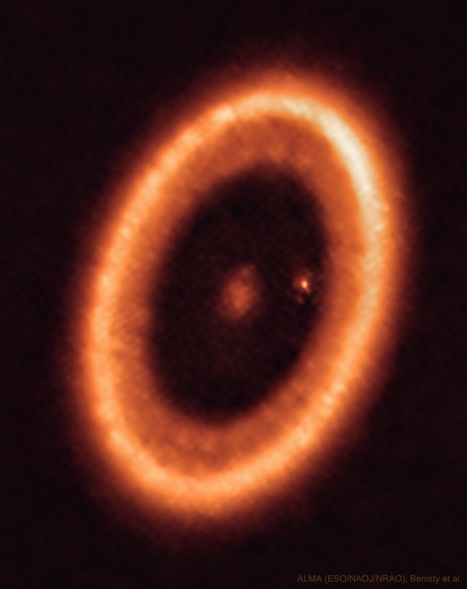 Im Bild ist ein orange leuchtender Ring, er ist leicht gekippt und daher nicht rund, sondern oval. In der Mitte leuchtet ein schwacher größerer Fleck und ein kleiner heller Fleck auf der 3-Uhr-Position.