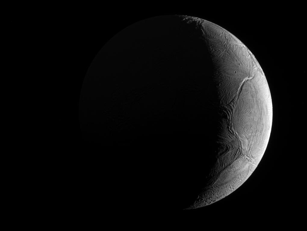 Vor dunklem Hintergrund leuchtet rechts die Sichel des Eismondes Enceladus.