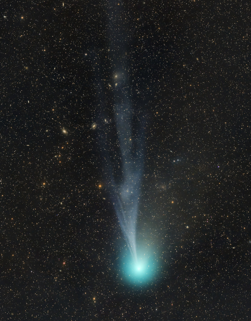 Vor einem sternklaren Hintergrund zieht ein Komet. Unten im Bild ist seine türkisgrüne Koma, nach oben breitet sich ein weißlicher, strukturierter Schweif aus.