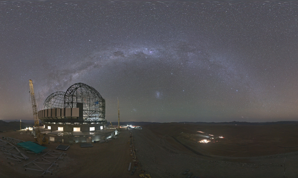 Auf einer dunklen Ebene steht das von innen beleuchtete Gerüst des Riesenteleskops ELT, dahinter wölbt sich am dunklen Himmel die Milchstraße.