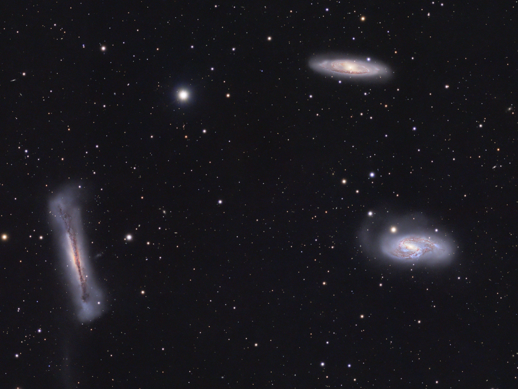 Drei Galaxien schweben vor einem dunklen Hintergrund mit wenigen Sternen. Links sehen wir eine fluffige Galaxie von der Kante, sie hat einen sehr breiten Rand, rechts oben und unten sind zwei kleinere Spiralgalaxien schräg von oben zu sehen.