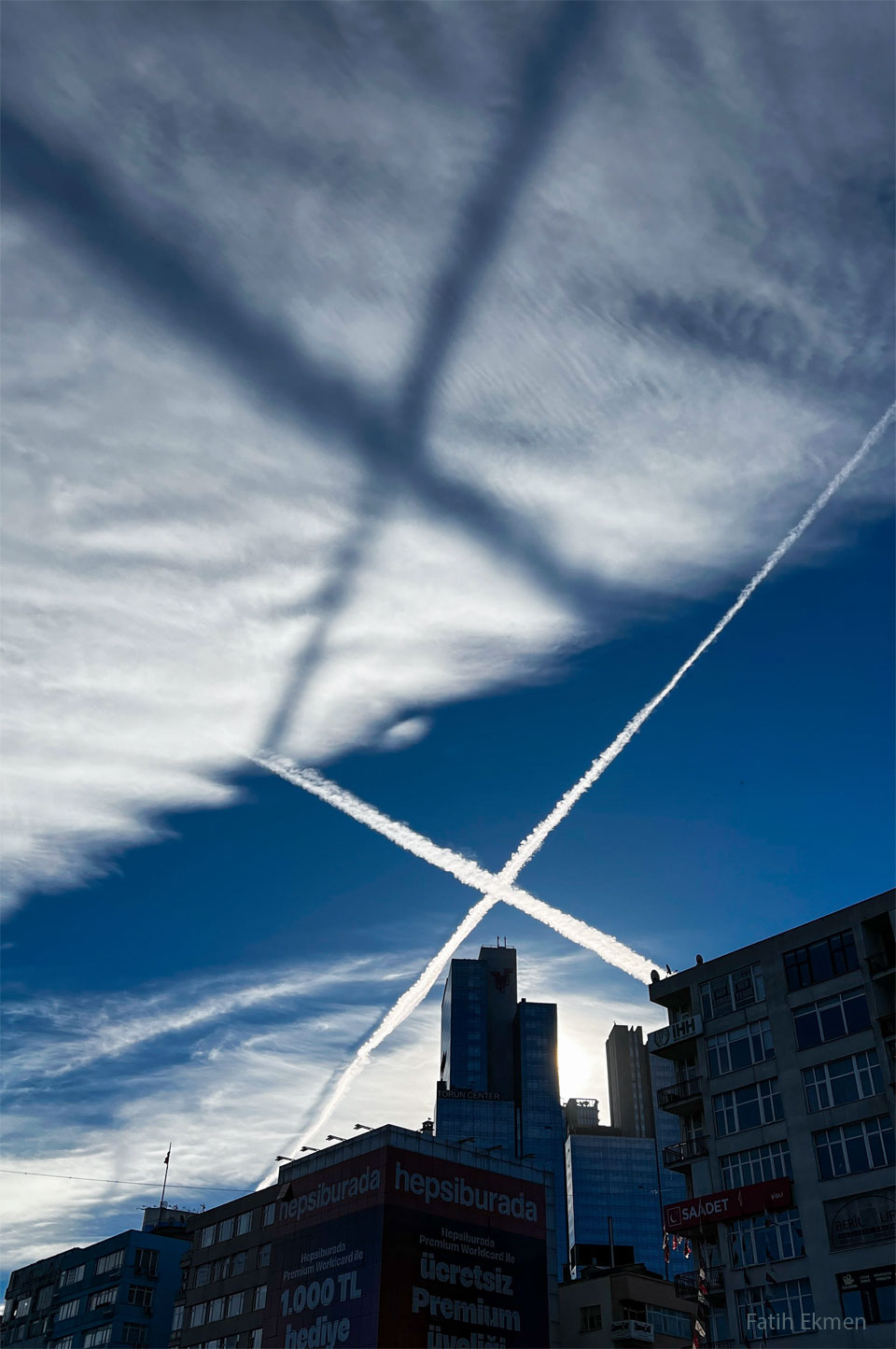 Am Himmel leuchtet ein riesiges X aus Kondensstreifen. Diese werfen einen X-förmigen Schatten auf die Wolken darüber.