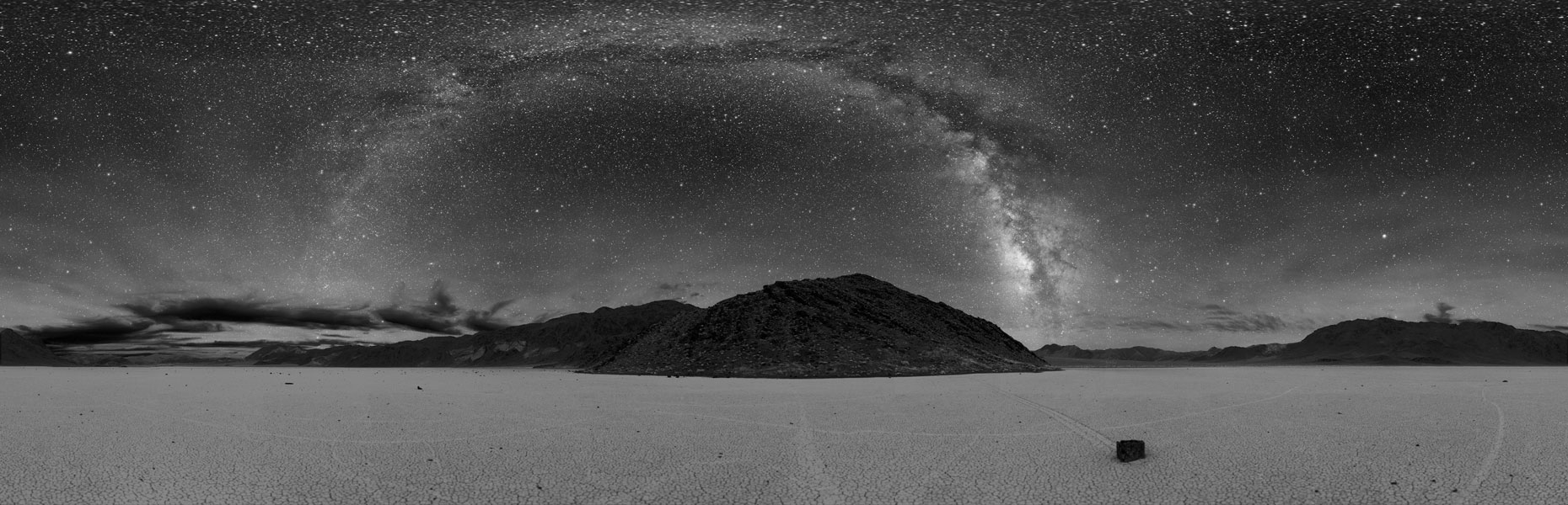 Über einem Panorama mit glatten Wüstenboden und Bergen im Hintergrund wölbt sich die Milchstraße.