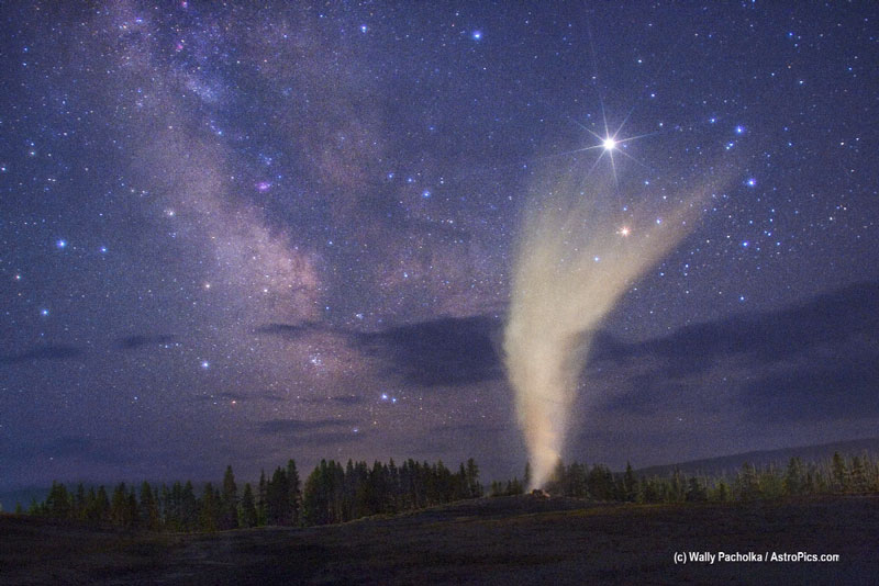 Der Geysir Old Faithful im Yellowstone Nationalpark bricht alle paar Minuten aus, im Hintergrund leuchten die Milchstraße und der Planet jupiter.