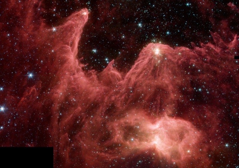 Rote Berge aus Staub und Gas türmen sich im Bild auf. Sie wurden von einem Stern geformt, der rechts oben außerhalb des Bildes leuchtet.