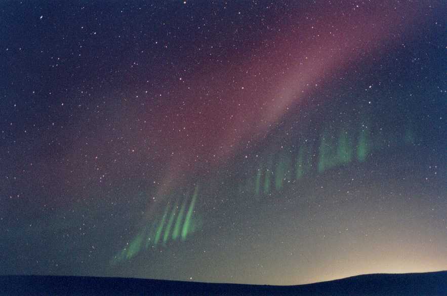 Am strnklaren Horizont leuchtet ein Polarlicht, oben eine gleichmäßige rote Wolke, unten grüne Streifen, die an einen Lattenzaun erinnern.