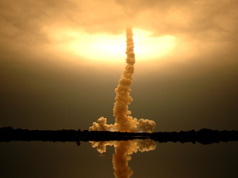 Das Bild zeigt eine Abgasschwade, die nach dem Start der Raumfähre Endeavour noch in der Luft hängt. Über den Wolken leutet es hell von den Triebwerken der Raumfähre.