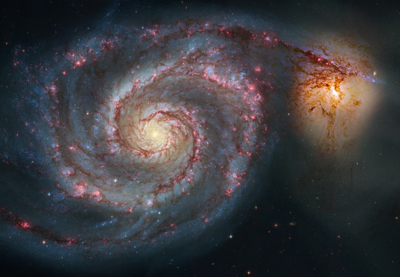 Die Strudelgalaxie M51 ist von oben zu sehen, rechts neben der großen Spiralgalaxie ist eine kleine Galaxie über einen Arm verbunden.